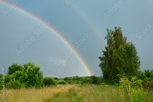 Rural scene with nature after the rain with double rainbow in the dark sky. Horizontal image.