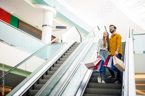 Full length body size view of her she his he nice attractive lovely cheerful couple shopping visiting retail store city building standing on escalator carrying new things life lifestyle