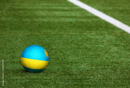 Rwanda flag on ball at soccer field background. National football theme on green grass. Sports competition concept.