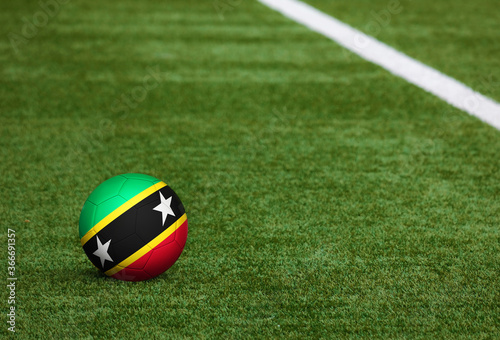 Saint Kitts And Nevis flag on ball at soccer field background. National football theme on green grass. Sports competition concept.
