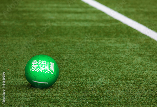 Saudi Arabia flag on ball at soccer field background. National football theme on green grass. Sports competition concept. photo