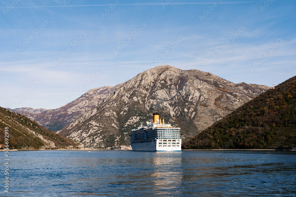 A tall, high-rise huge cruise liner in the Verige Strait, in the Boka Kottorska - Kotor Bay in Montenegro, against the backdrop of the city of Perast.
