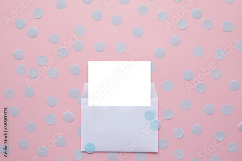 white blank card in white envelope on pink background with confetti. Holiday mockup. Top view. © producer