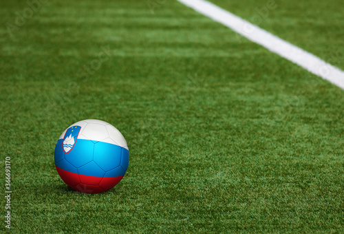 Slovenia flag on ball at soccer field background. National football theme on green grass. Sports competition concept.