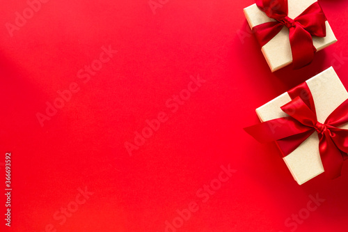 Two gift boxes with a red bow on a red background, top view with copy space