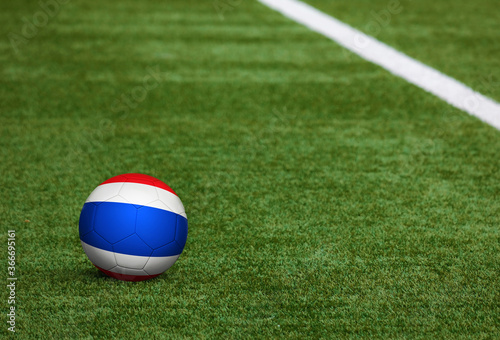 Thailand flag on ball at soccer field background. National football theme on green grass. Sports competition concept.