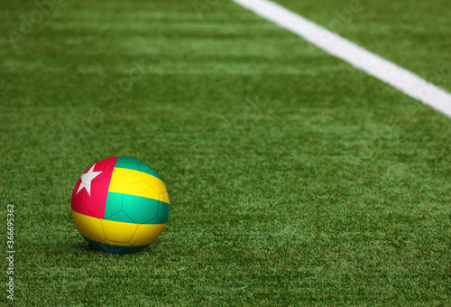 Togo flag on ball at soccer field background. National football theme on green grass. Sports competition concept.