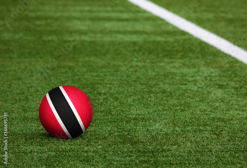 Trinidad And Tobago flag on ball at soccer field background. National football theme on green grass. Sports competition concept.