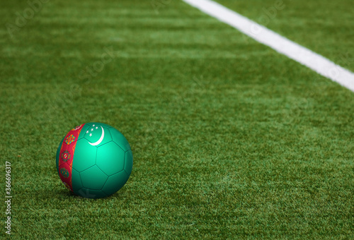 Turkmenistan flag on ball at soccer field background. National football theme on green grass. Sports competition concept.