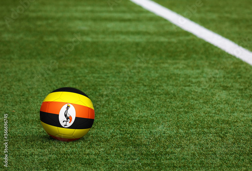 Uganda flag on ball at soccer field background. National football theme on green grass. Sports competition concept.