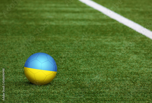 Ukraine flag on ball at soccer field background. National football theme on green grass. Sports competition concept.