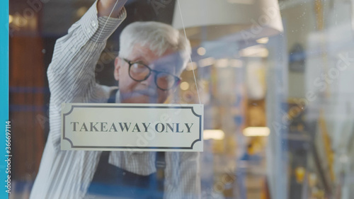 Senior male cafe owner hanging take out only sign on glass door