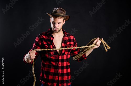 Lasso is used in rodeos as part of competitive events. Lasso can be tied or wrapped. Western life. Man unshaven cowboy black background. Man wearing hat hold rope. Lasso tool of American cowboy