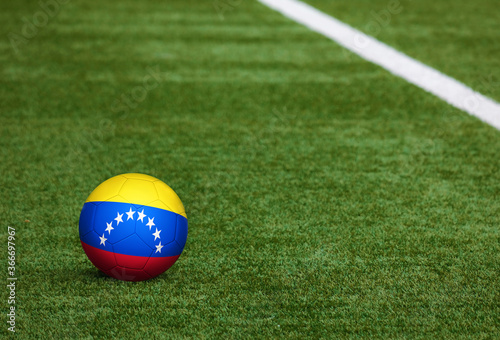 Venezuela flag on ball at soccer field background. National football theme on green grass. Sports competition concept.