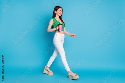 Full body profile side photo of positive cheerful girl hold takeout coffee cup go walk copyspace wear tank-top sandals isolated over blue color background