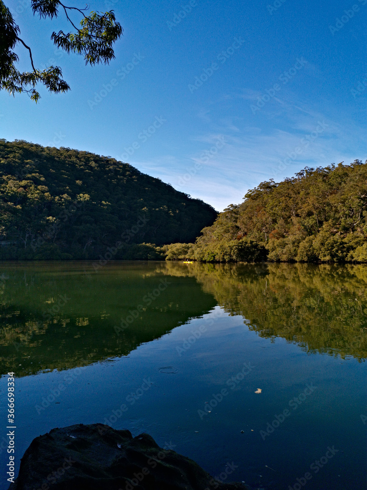 Early morning view of a calm creek with beautiful reflections of blue sky, mountains and trees on water, Cowan Creek, Bobbin Head, Ku-ring-gai Chase National Park, New South Wales Australia Early morning view of a calm creek with beautiful reflections of blue sky, mountains and trees on water, Cowan Creek, Bobbin Head, Ku-ring-gai Chase National Park, New South Wales Australia