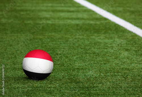 Yemen flag on ball at soccer field background. National football theme on green grass. Sports competition concept.
