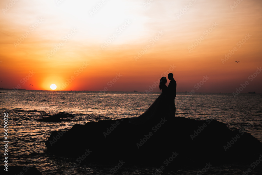 Wedding couple kissing and hugging on rocks near blue sea