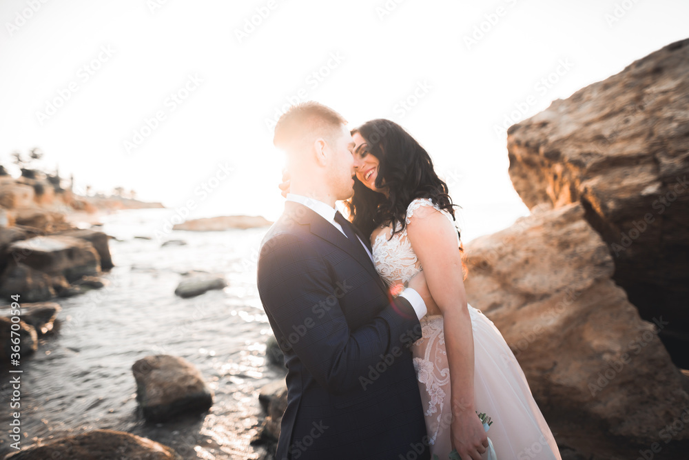 Fototapeta premium Wedding couple, groom, bride with bouquet posing near sea and blue sky