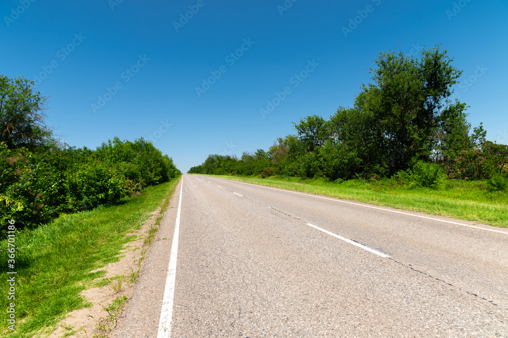 suburban empty road asphalt surrounded by trees and grass. The concept of transportation and travel. Background green grass asphalt and blue sky suburban empty road asphalt surrounded by trees and grass. The concept of transportation and travel. Background green grass asphalt and blue sky
