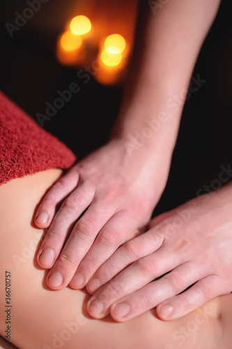 Close-up professional massage of the female hip in the dark room of the spa salon against the background of burning candles. The concept of hip muscle health