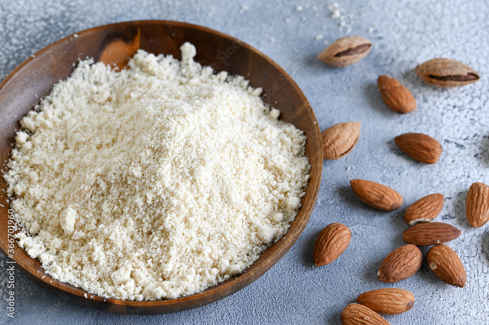 Almond flour in a wooden bowl, almonds on old light background Almond flour in a wooden bowl, almonds on old light background