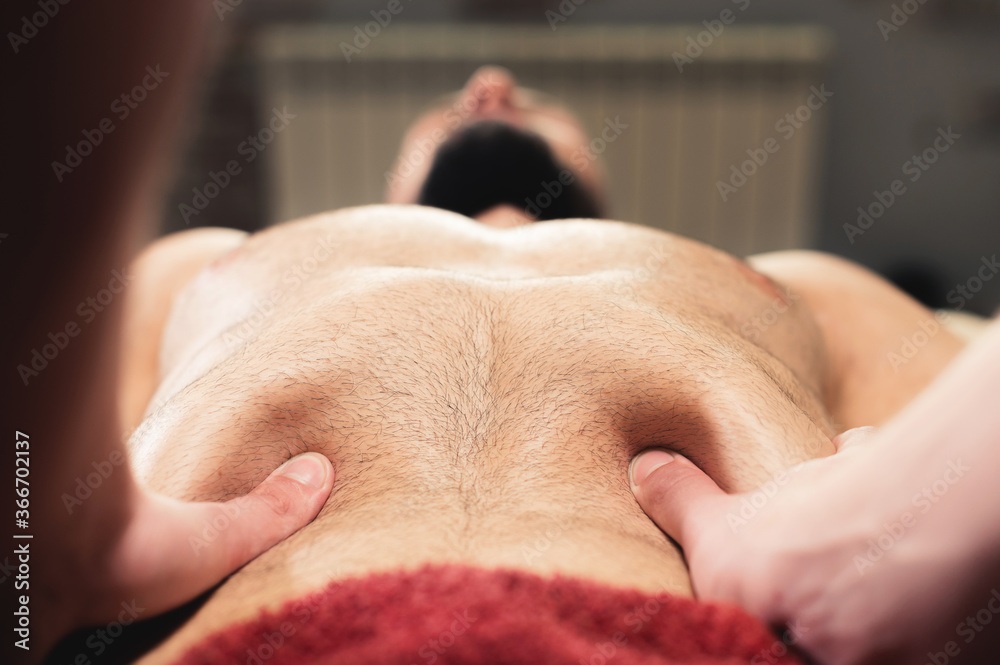 Naklejka premium Close-up professional massage of the diaphragm to a man in a professional massage room. The concept of internal organs and abdominal cavity