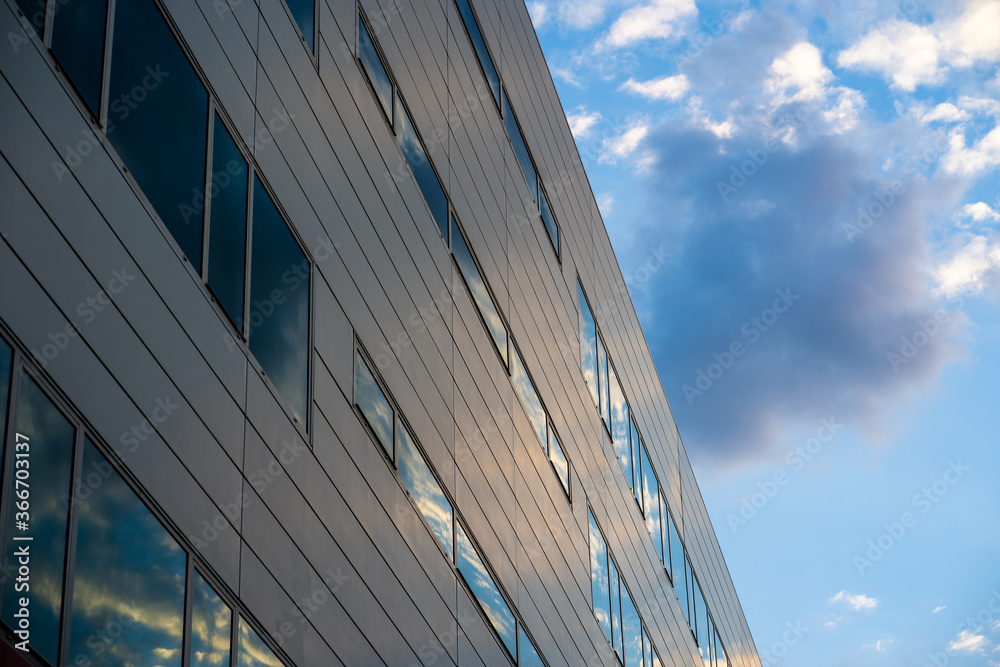 Fachada de un edificio de oficinas cuyas ventanas reflejan el cielo con ...