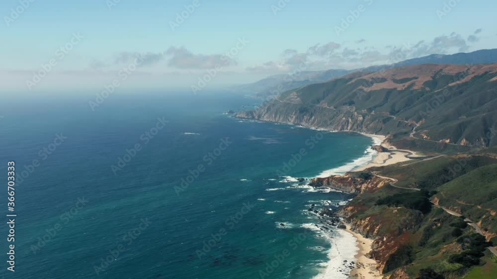 Most scenic stretch of undeveloped coastline in USA, known as Big Sur. 4K Stunning aerial view over the rocky ocean coast. Beautiful ocean water of various shades of blue meets the mountains shore.