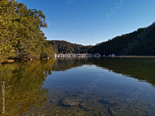 Early morning view of a creek with beautiful reflections of blue sky  boats  mountains and trees on water  Cowan Creek  Bobbin Head  Ku-ring-gai Chase National Park  New South Wales Australia
