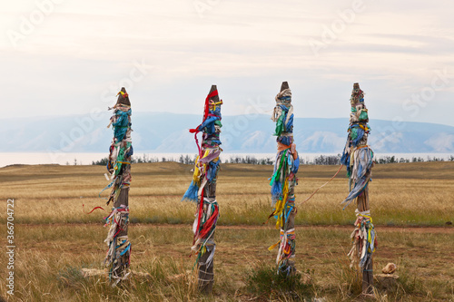 Baikal Lake. Olkhon Island. The pillars with prayer flags and colored ribbons near the dirt road for Hoboy Cape at summer day