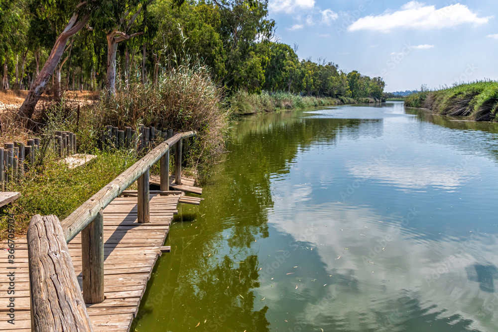 Pier on the Alexander River in Israel with eucalyptus trees along the banks and the reflection of clouds in the water