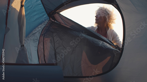 Foto View from inside of tent of mature woman traveler unzipping tent door and taking