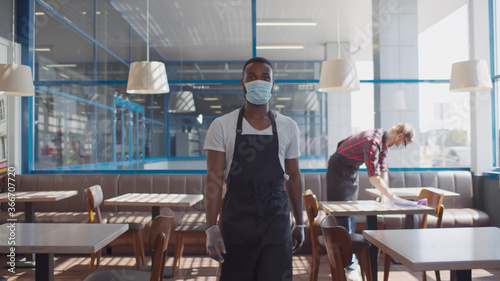Portrait of african waiter in apron safety mask and glves walking in cafe