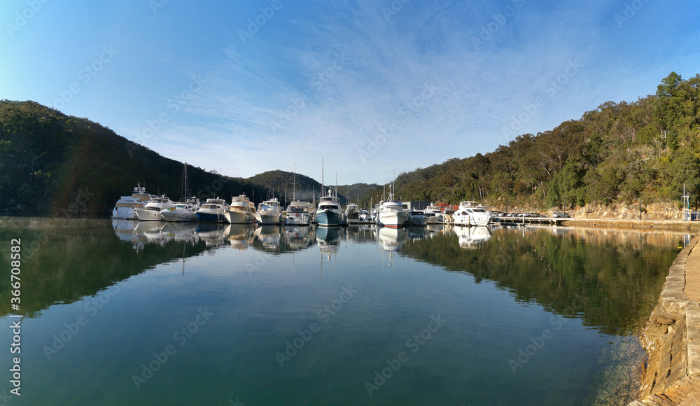 Early morning view of a creek with beautiful reflections of blue sky, luxury boats, mountains and trees on water, Cowan Creek, Bobbin Head, Ku-ring-gai Chase National Park, New South Wales Australia