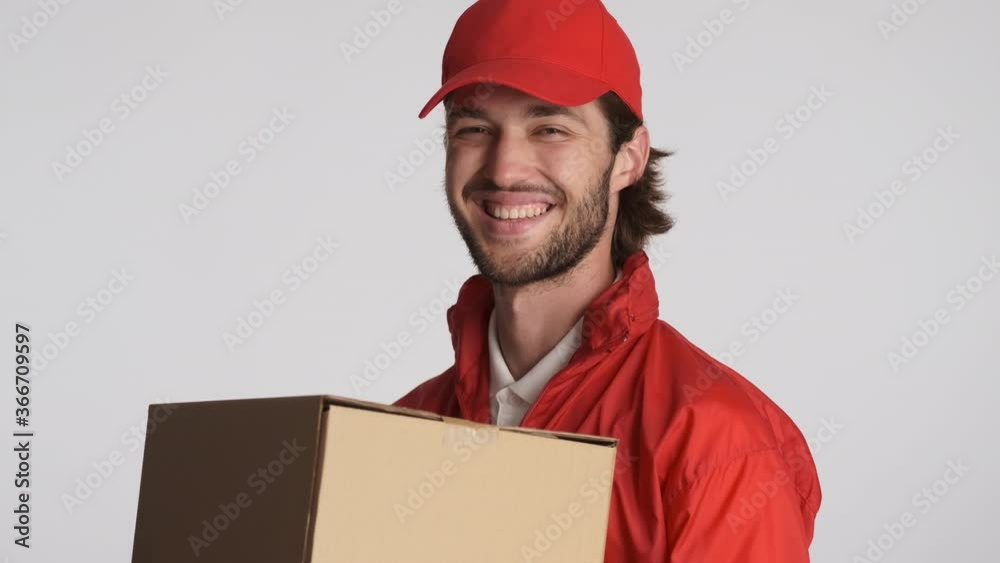 Attractive cheerful courier man in red cap and jacket holding delivery boxes joyfully looking in camera isolated. Service concept Attractive cheerful courier man in red cap and jacket holding delivery boxes joyfully looking in camera isolated. Service concept