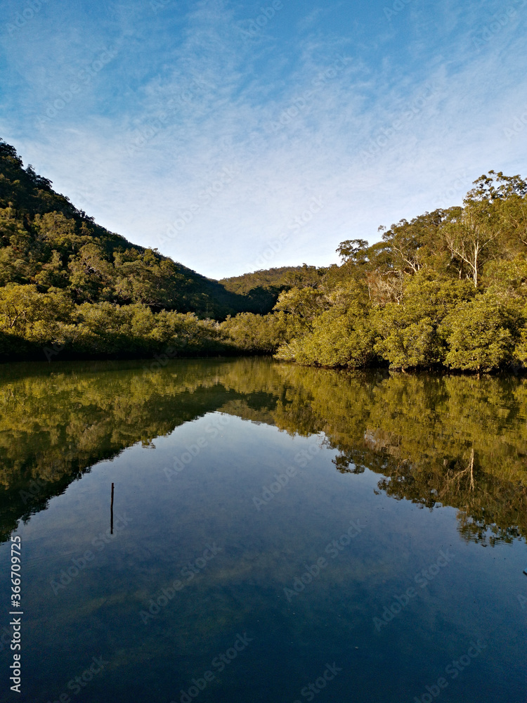 Early morning view of a calm creek with beautiful reflections of blue sky, mountains and trees on water, Cockle Creek, Bobbin Head, Ku-ring-gai Chase National Park, New South Wales Australia