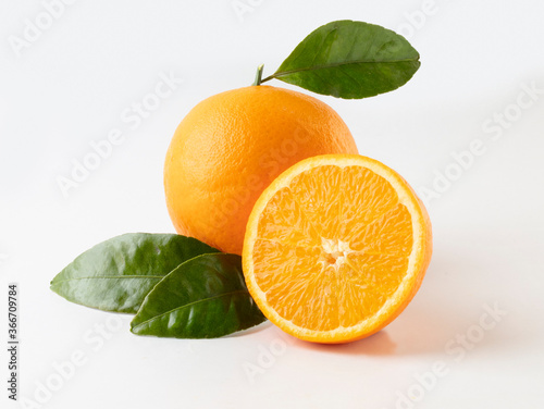 naranja entera y partida con hojas sobre fondo blanco. whole orange and split with leaves.