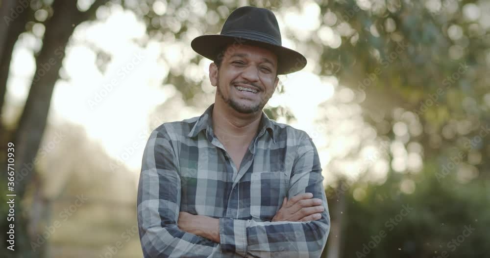 Portrait of young man with crossing hands in the hat and casual shirt in the farm on the colorful sky background. 4K. Portrait of young man with crossing hands in the hat and casual shirt in the farm on the colorful sky background. 4K.