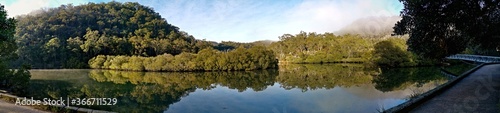 Early morning panoramic view of a creek with beautiful reflections of blue sky, fog, mountains and trees on water, Cockle Creek, Bobbin Head, Ku-ring-gai Chase National Park, New South Wales Australia
