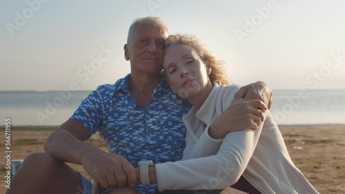 Loving senior couple hugging looking at each other sitting on sea beach outdoor