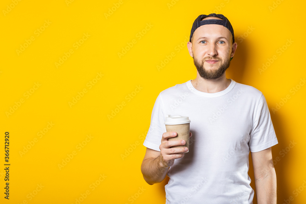 Friendly young man holding a paper cup of coffee on yellow background. Friendly young man holding a paper cup of coffee on yellow background.