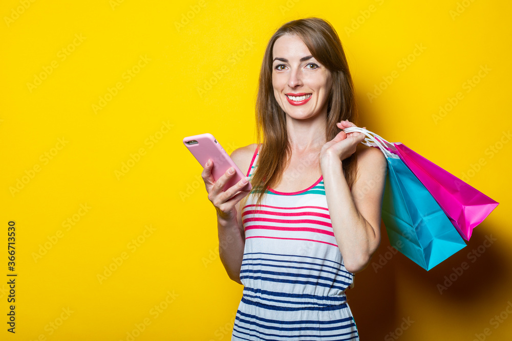 Beautiful smiling young woman with phone and shopping bags on yellow background. Beautiful smiling young woman with phone and shopping bags on yellow background.