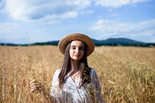 Portrait of a girl in a wheat field. Portrait of a beautiful girl in a white dress and hat on a wheat field. Girl in a white dress and hat. Wheat field. Portrait of a young woman in nature.
