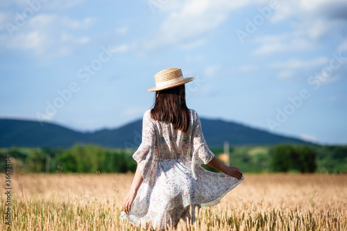 Portrait of a girl from the back in a wheat field. Portrait of a beautiful girl in a white dress and hat on a wheat field. Girl in a white dress and hat. Wheat field.