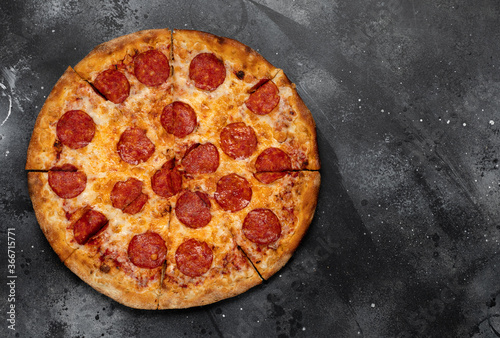 Pepperoni pizza on black concrete background. Top view with copy space. Tasty sliced pepperoni pizza