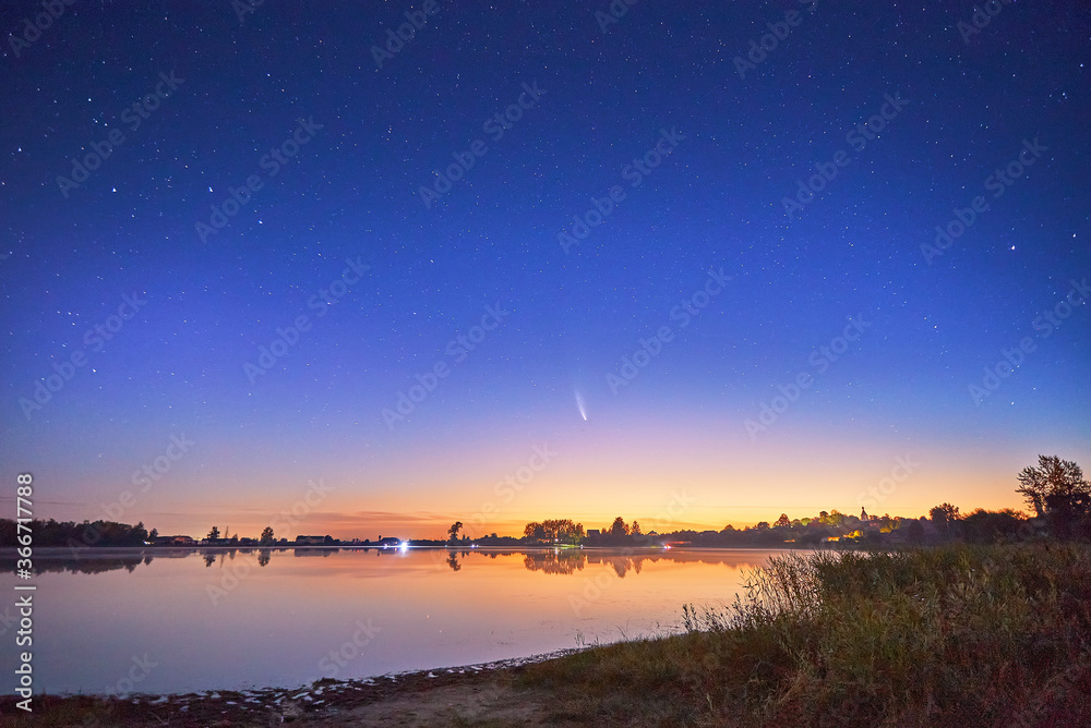 Neowise comet with light tail in night sky over lake