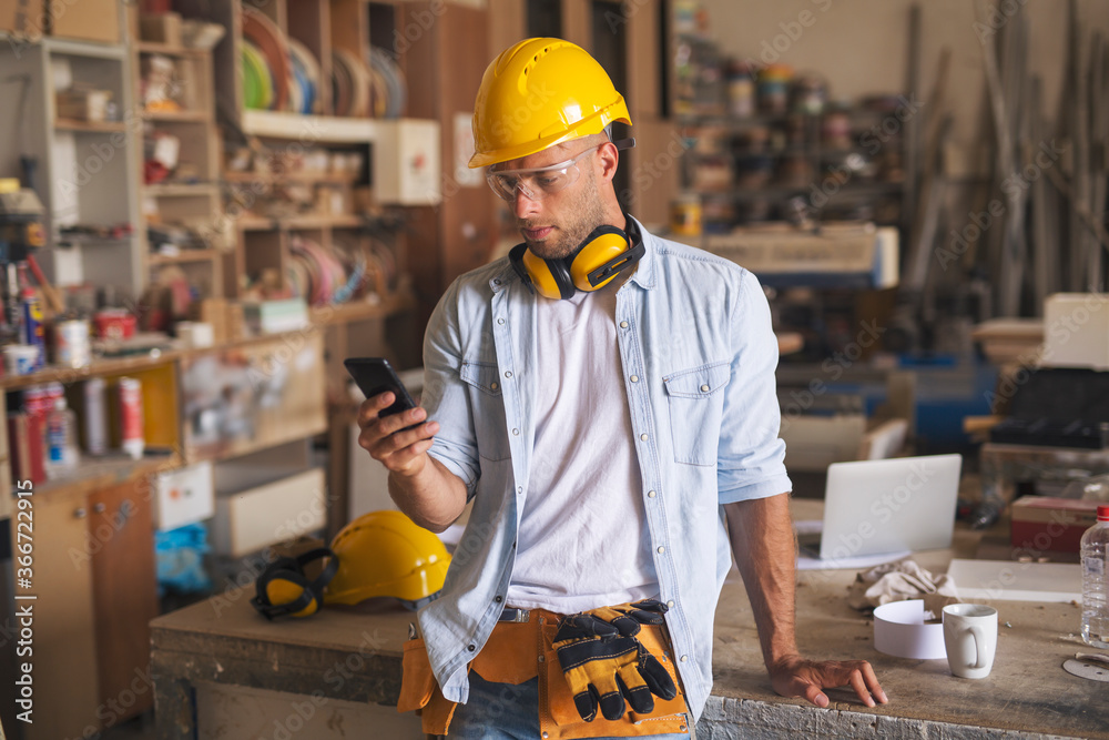 Young carpenter with a serious look on his face looking at smartphone Young carpenter with a serious look on his face looking at smartphone