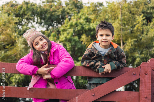 Children standing on a wooden fence.  They enjoy a sunny day outdoors.  It's an autumn day.