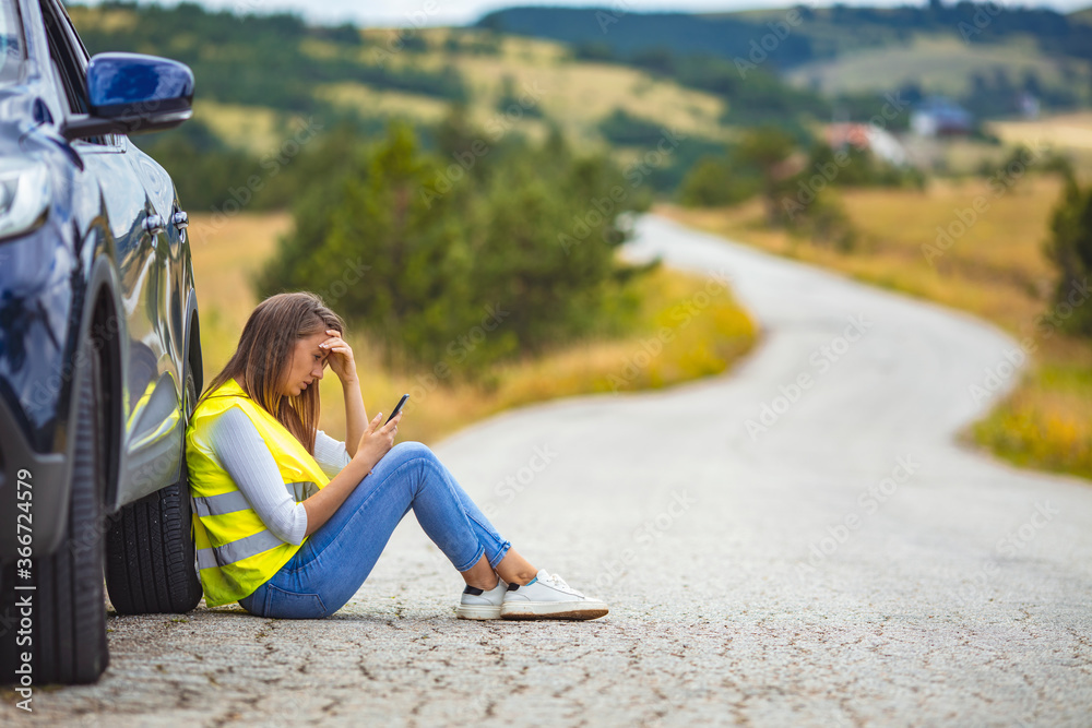 Young woman standing by her broken car on the road and using phone to call for help. Hello, I have a problem with my car! Young Woman calling for assistance with his car broken down by the roadside